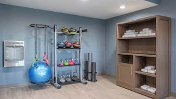 A gym with exercise equipment, a water dispenser, and a storage cabinet with towels.