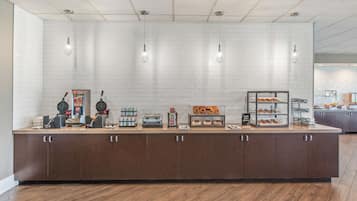 A breakfast bar with a variety of food items and appliances, including waffle makers, a coffee machine, and a display case with pastries.
