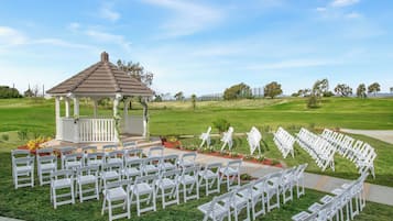 A gazebo with white chairs arranged in rows on a grassy lawn.