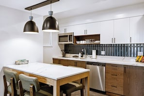 A modern kitchen with white cabinets, a stainless steel dishwasher, and a marble countertop.