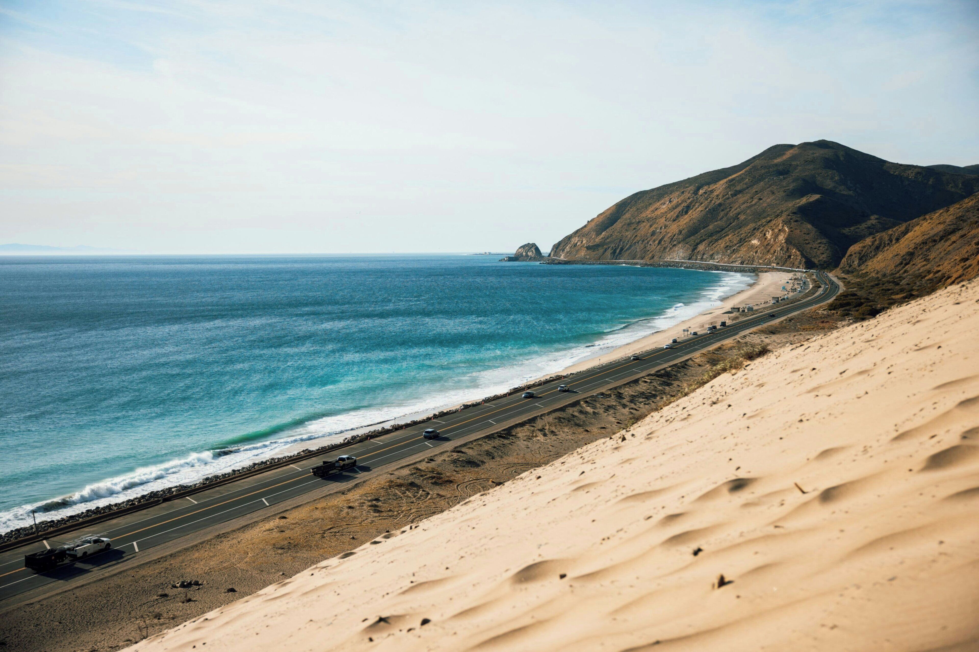 Una carretera costera con una playa y una montaña al fondo.