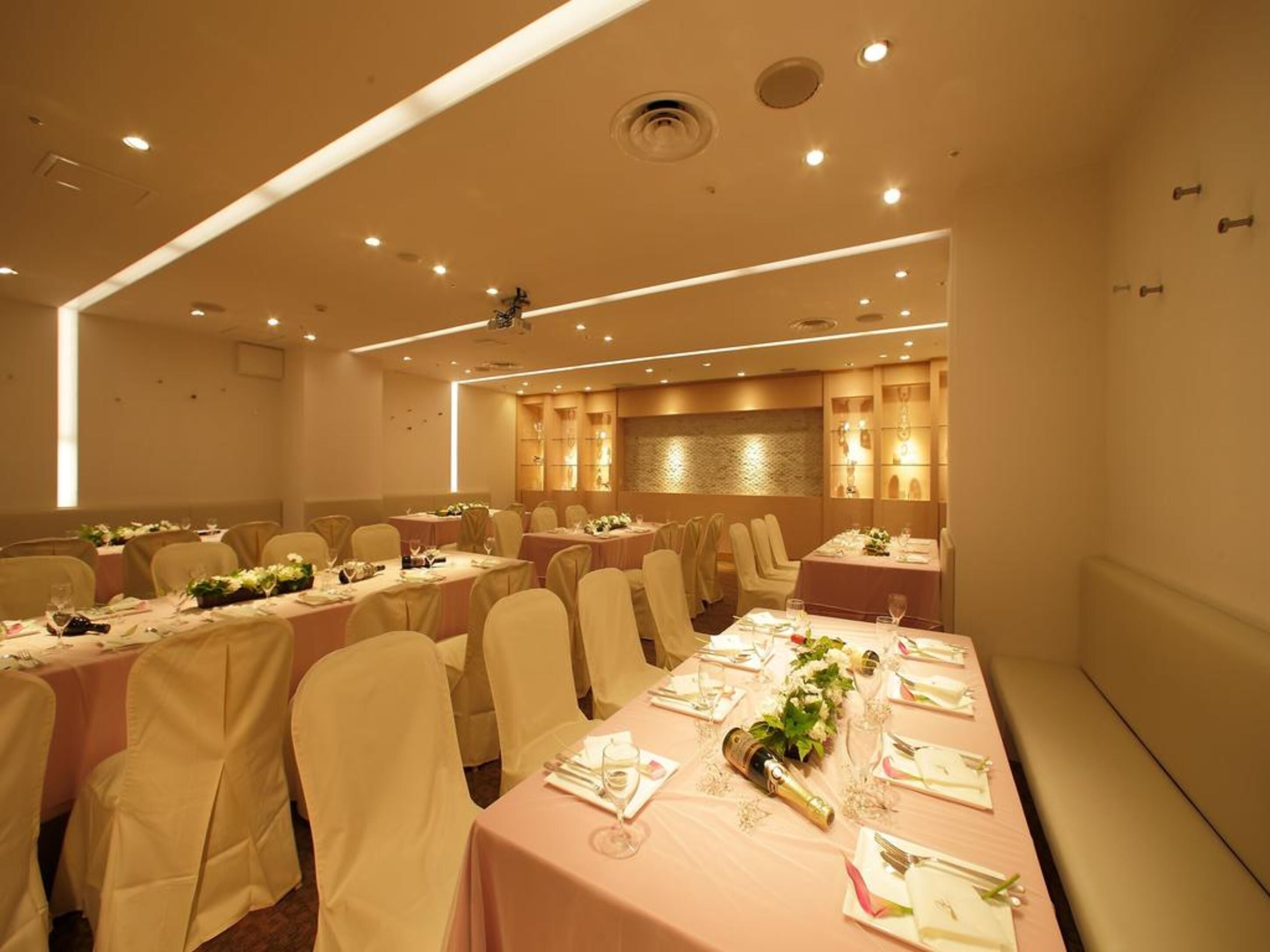 A banquet hall with multiple round tables, each set with white tablecloths, chairs, and floral centerpieces.