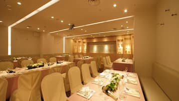 A banquet hall with multiple round tables, each set with white tablecloths, chairs, and floral centerpieces.