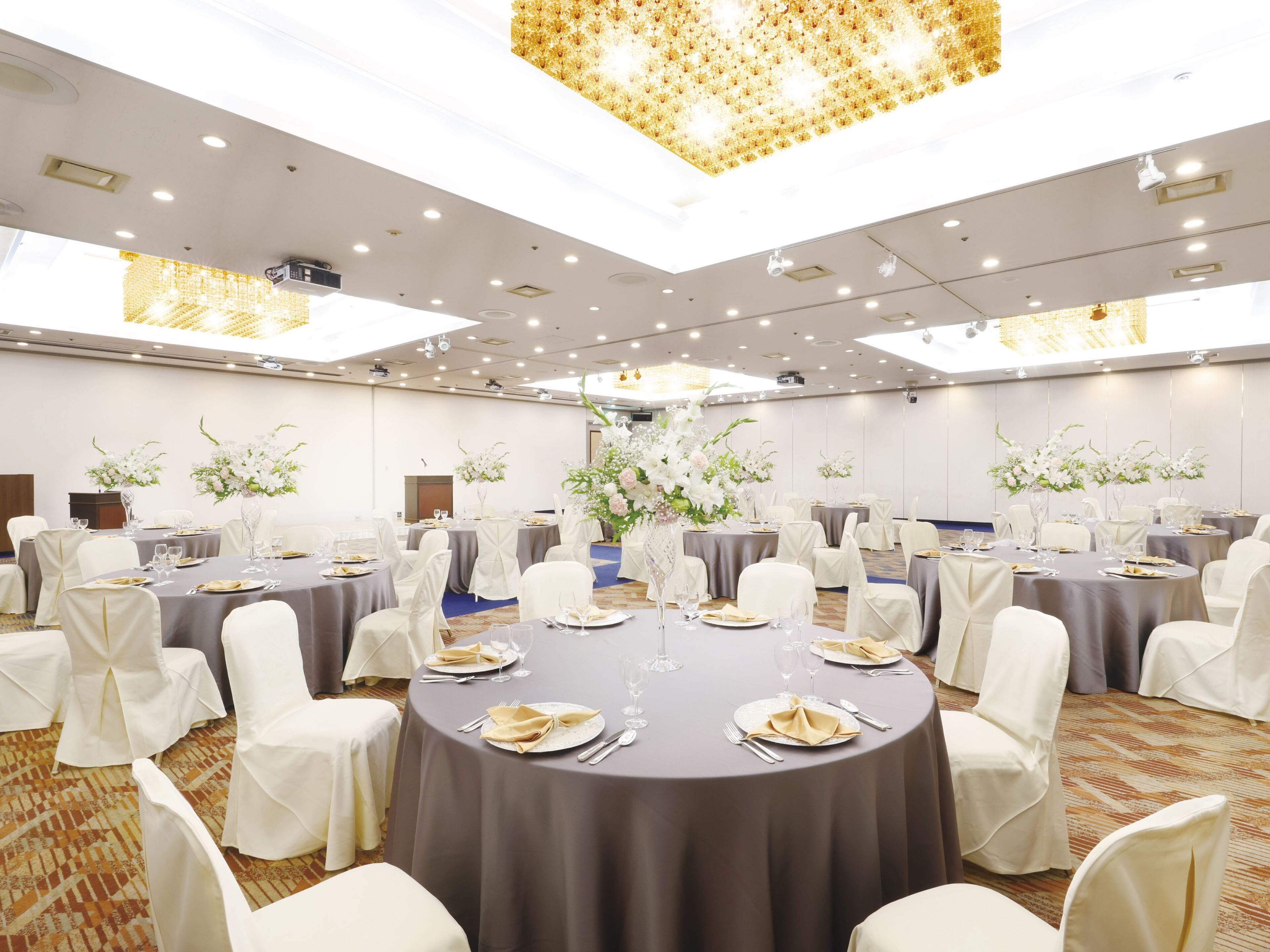 A banquet hall with round tables, white chairs, and floral centerpieces.