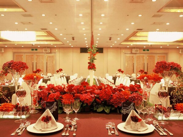 A banquet hall with tables set for a formal event, featuring red floral centerpieces and elegant tableware. - ART HOTEL Kagoshima (Kagoshima)