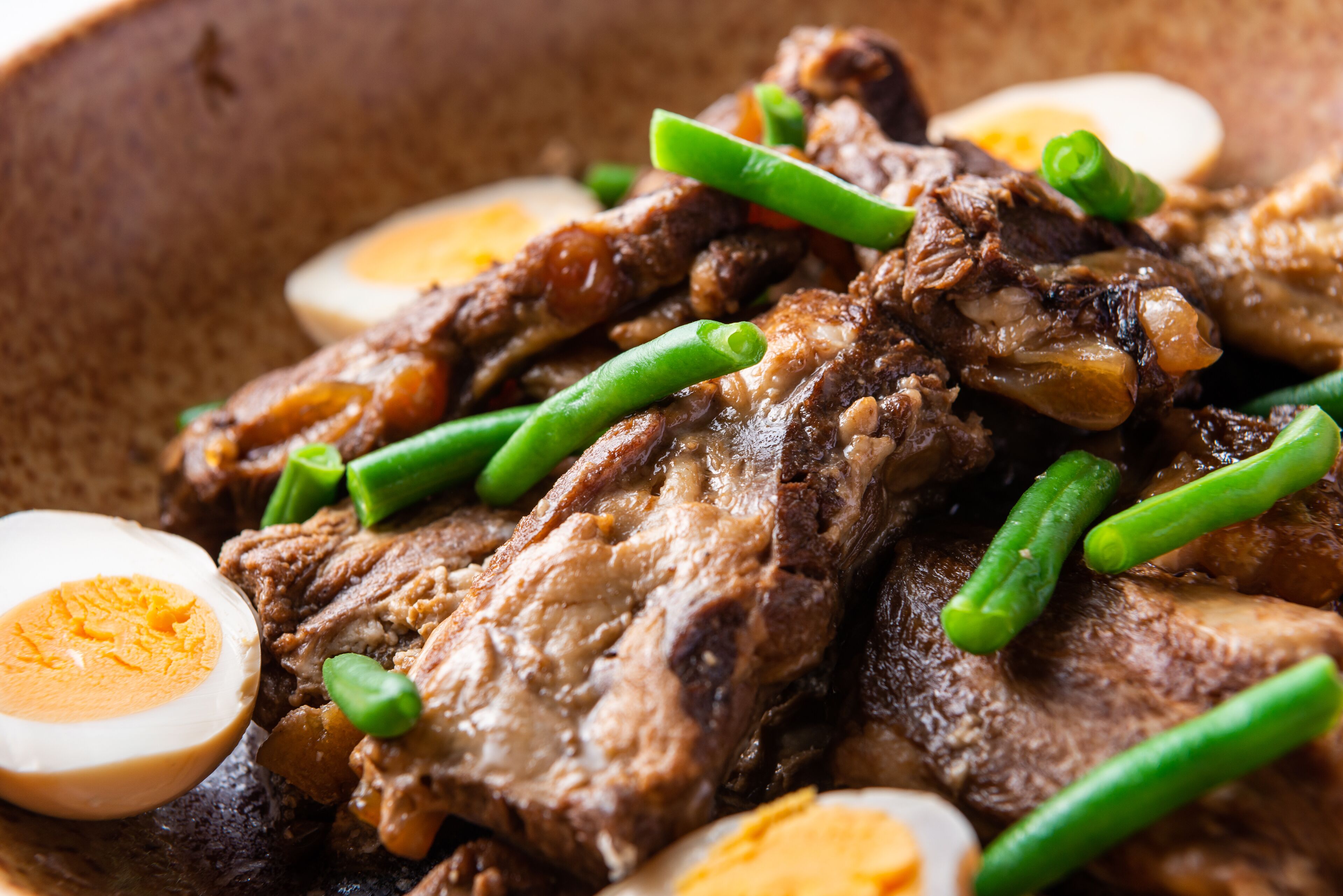 A close-up of a dish with meat, green beans, and halved boiled eggs.