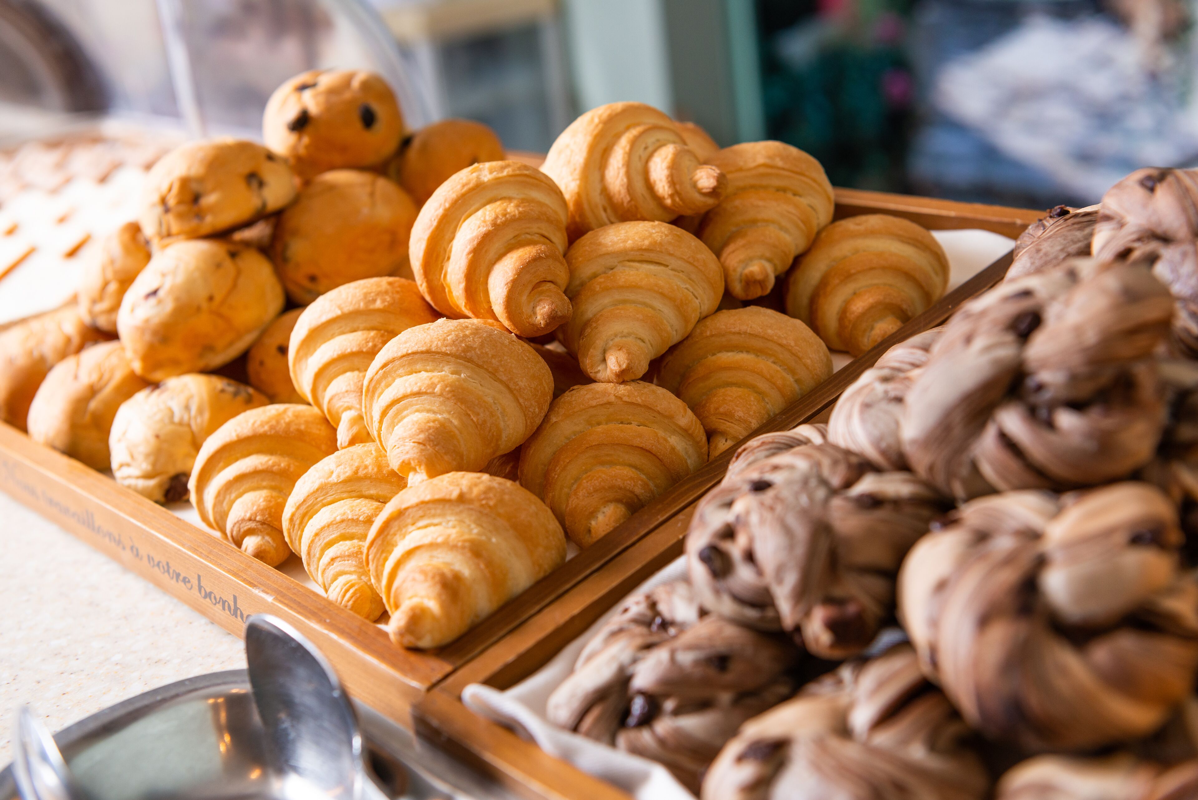 Une variété de pâtisseries, notamment des croissants et des biscuits aux pépites de chocolat, présentées sur un plateau en bois.