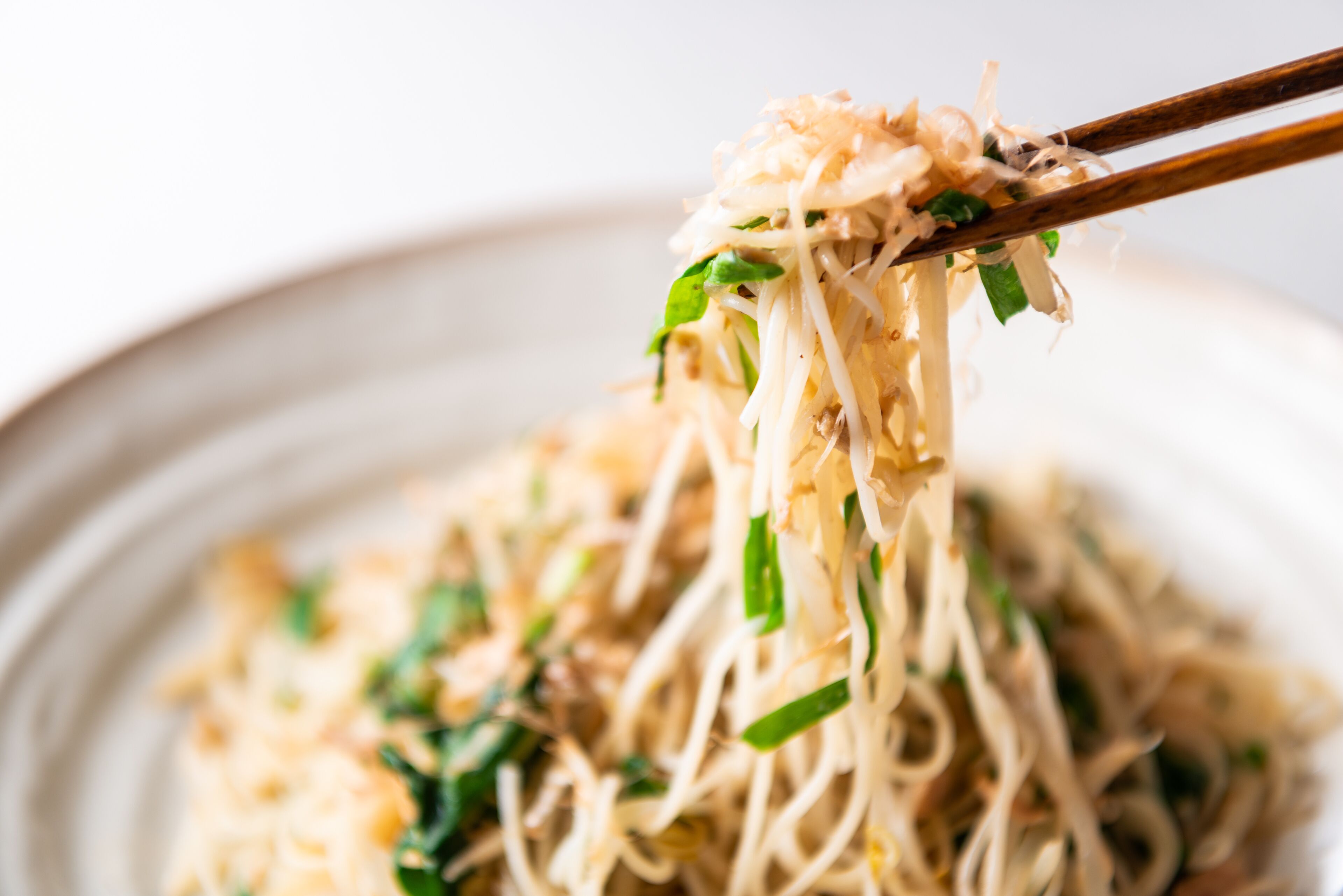 A close-up of a noodle dish with chopsticks lifting noodles, garnished with green onions.
