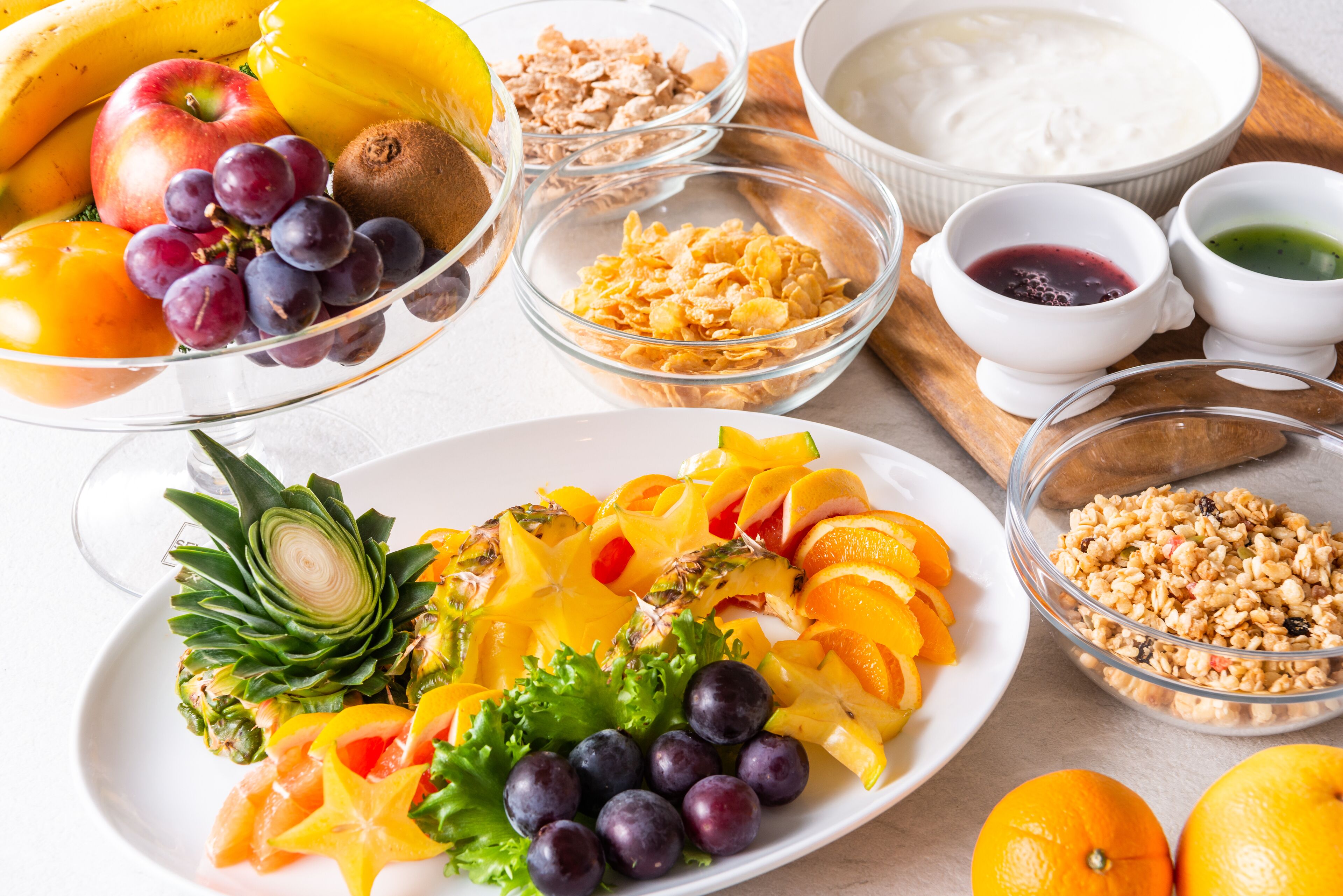 Variedad de frutas y alimentos sobre una mesa, como manzanas, plátanos, uvas, naranjas y una piña.