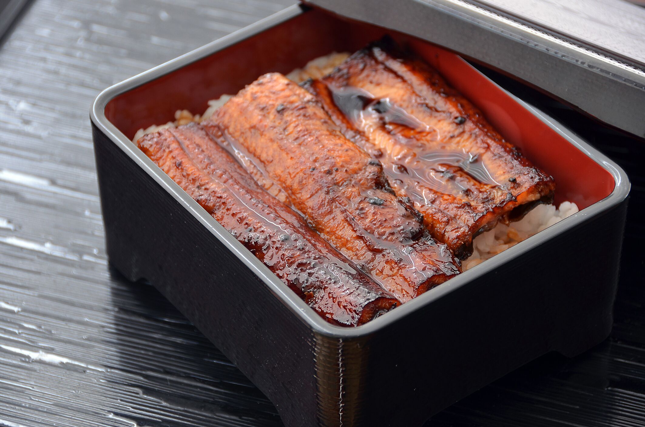 A tray of grilled salmon in a black container.