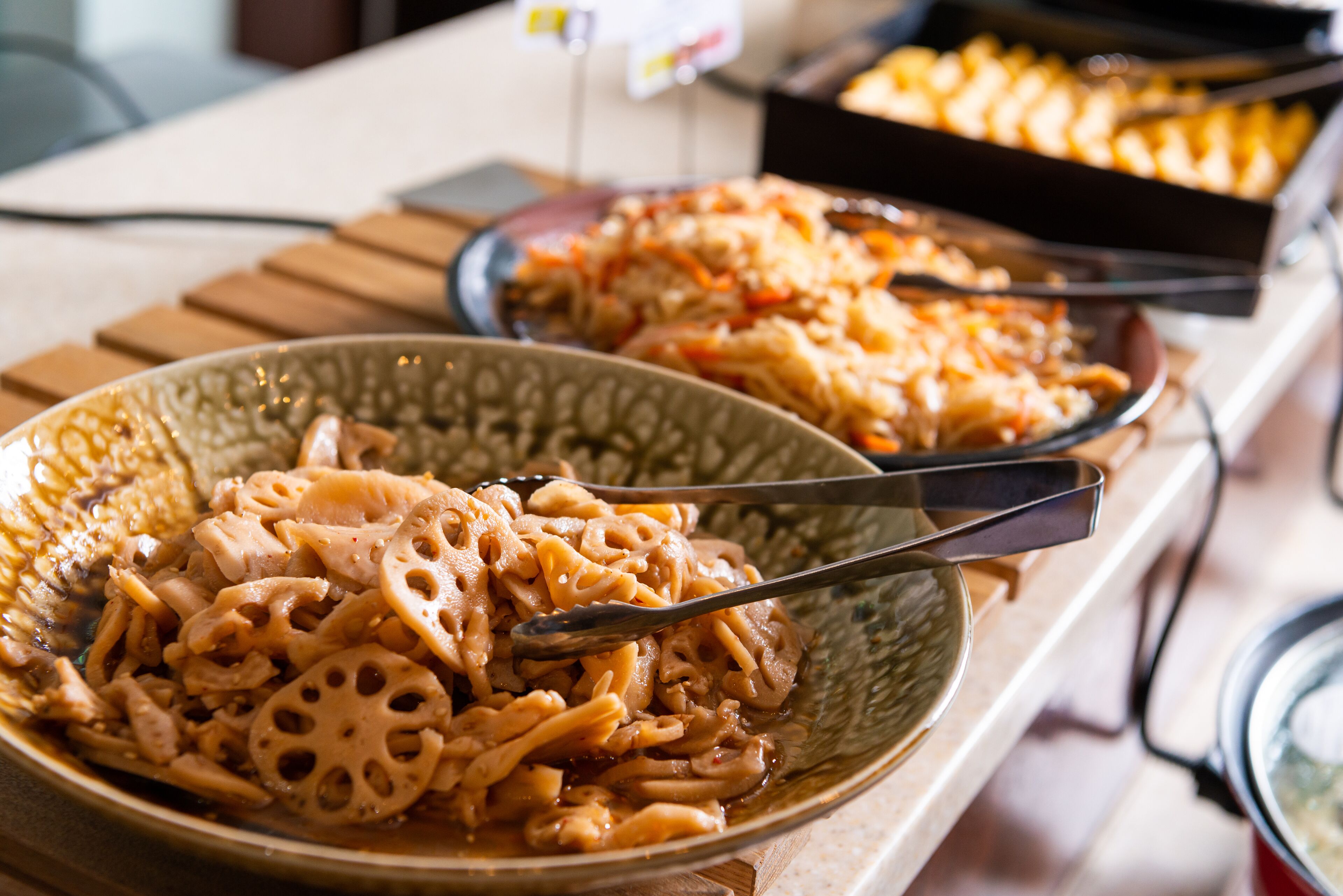 En buffet med forskellige retter, heriblandt pasta og en skål med grøntsager i skiver.
