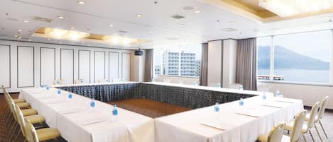 A conference room with a large table, chairs, and a view of a body of water and mountains.