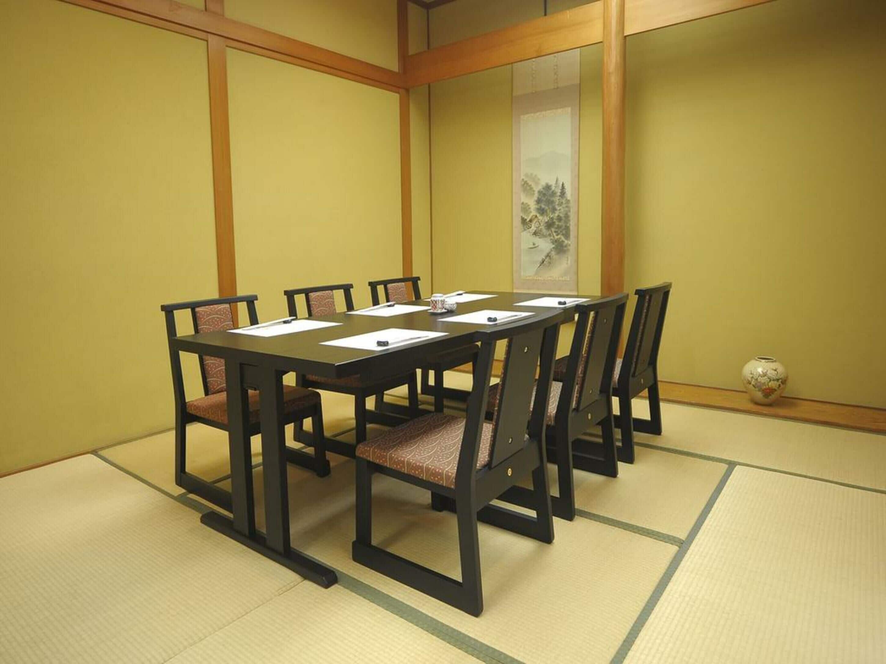 Ein traditioneller japanischer Besprechungsraum mit Tatami-Böden, einem niedrigen Tisch und dunklen Holzsesseln.
