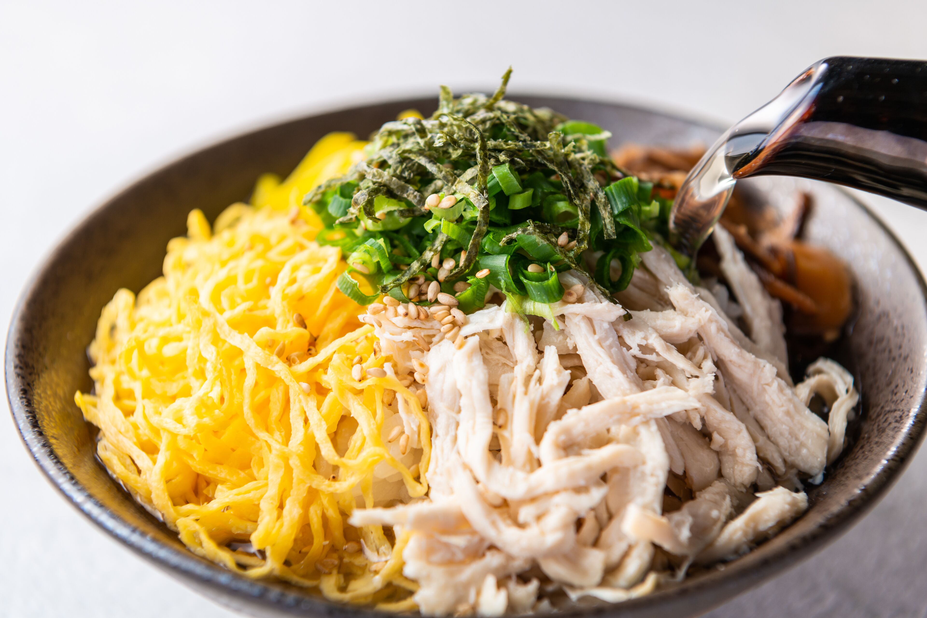 Uma tigela de ramen com macarrão, frango desfiado e cebolinha.