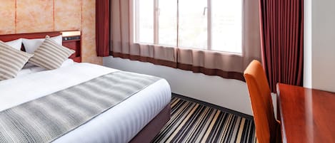 Een hotelkamer met een bed, bureau en een raam met gordijnen.