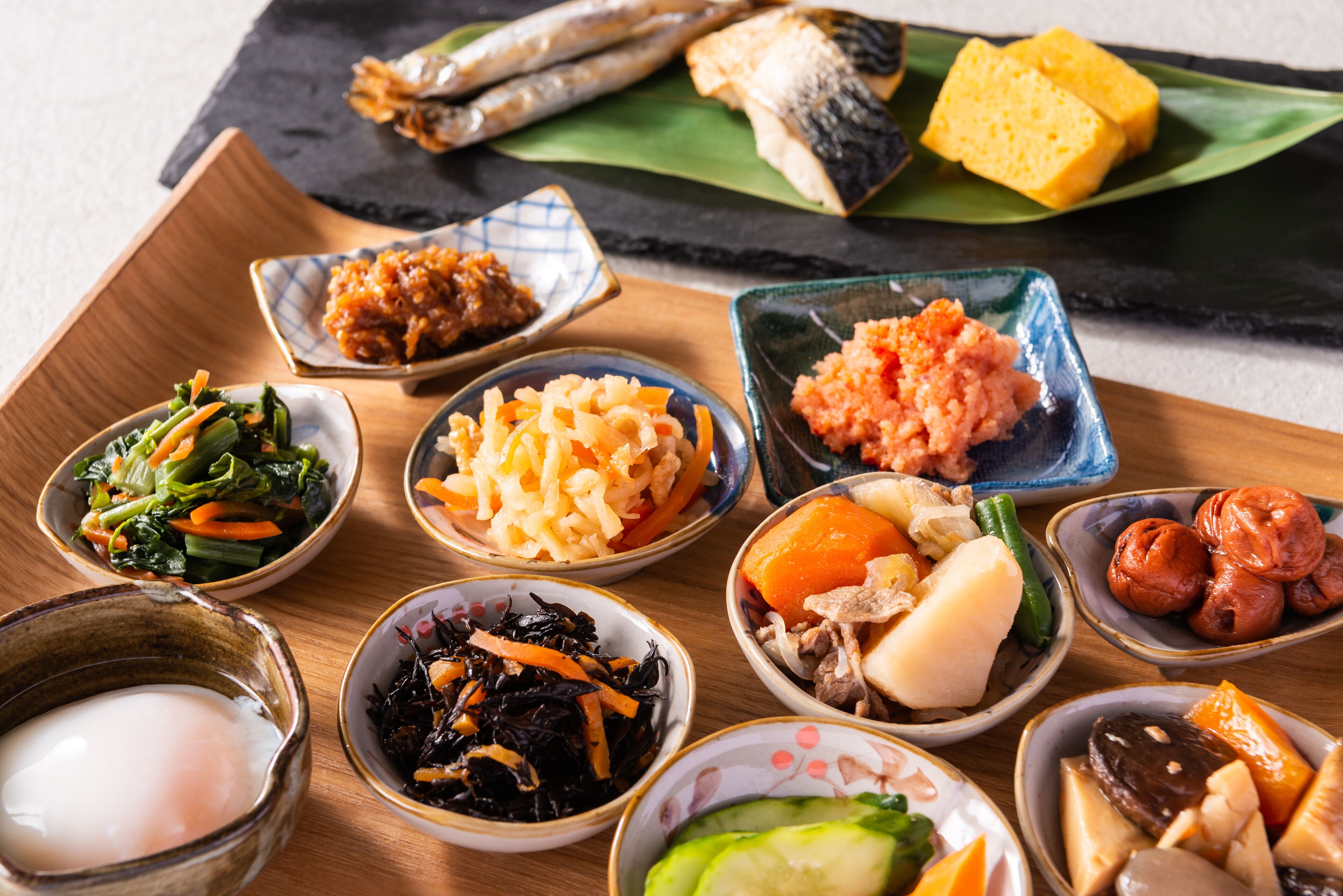 A variety of dishes on a wooden tray, including fish, vegetables, and other foods.