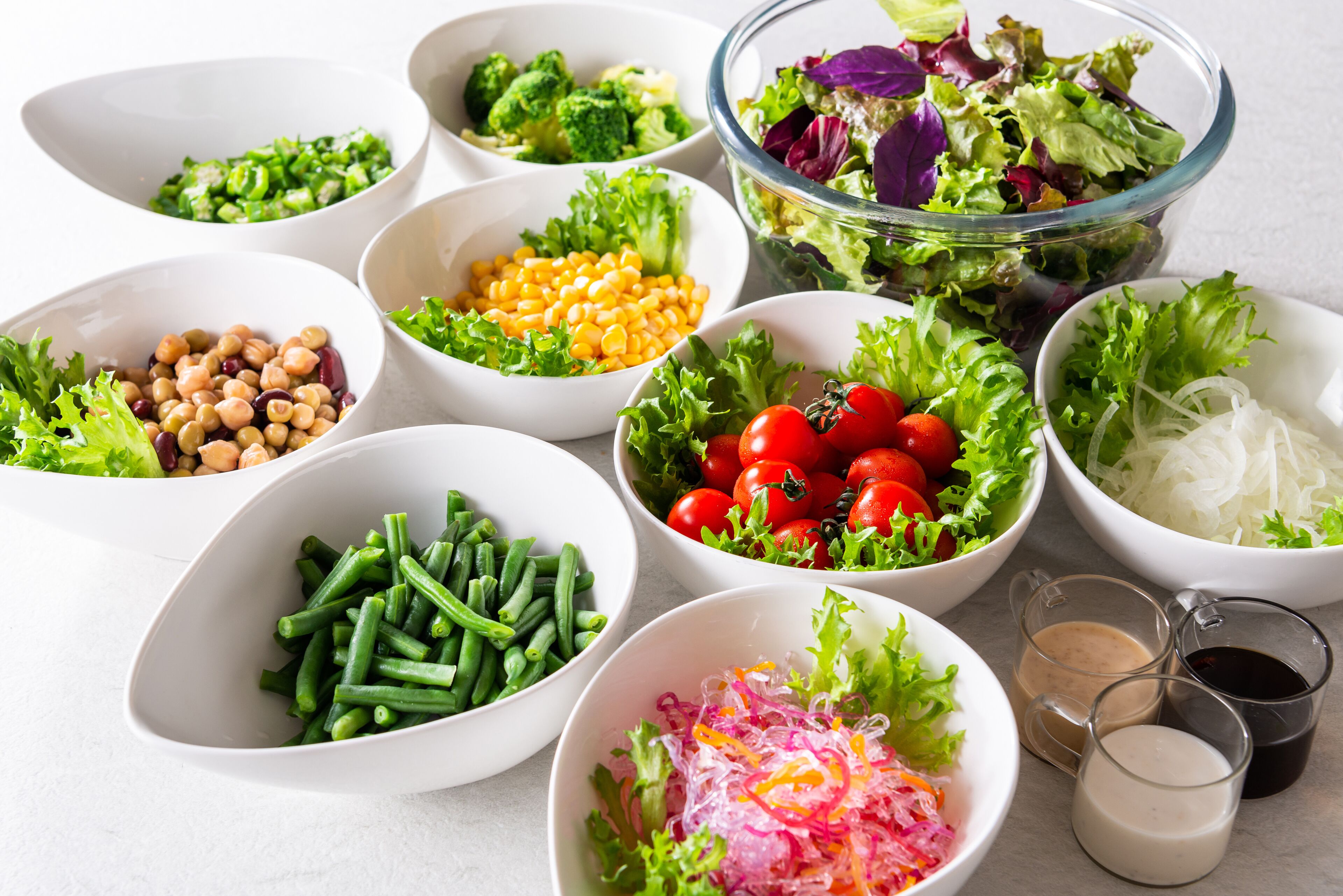 Différents bols contenant des ingrédients pour la salade, notamment de la laitue, des tomates, du maïs et des haricots.