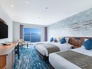 Habitación de hotel con dos camas, un escritorio, una silla, un televisor y un ventanal con vistas a montañas.