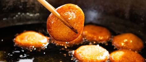 A close-up of a fried food item being lifted with chopsticks, surrounded by other similar items in a frying pan.