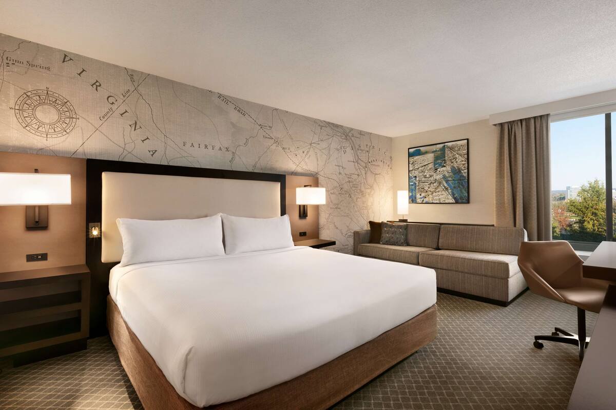 A hotel room with a large bed, a sofa, a desk, and a map on the wall.