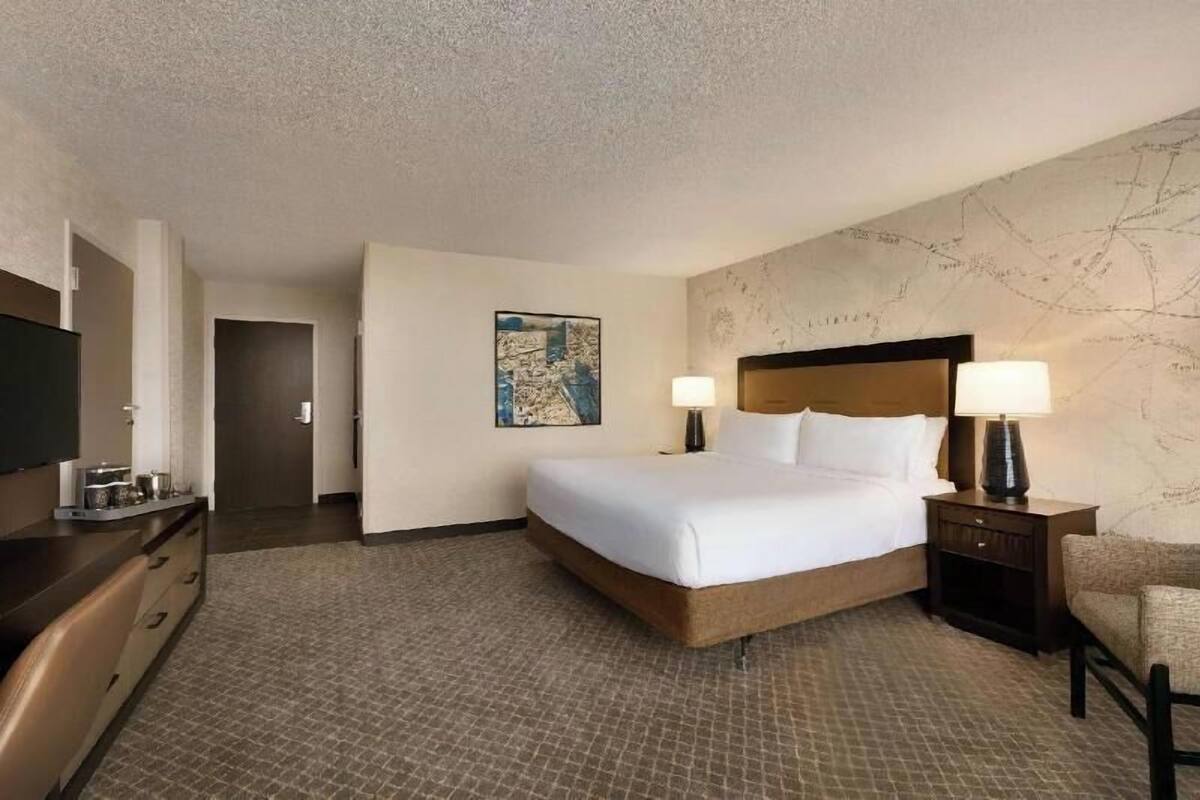 A hotel room with a large bed, two bedside lamps, a flat-screen TV, a desk with a chair, and a map on the wall.