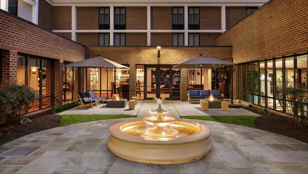 A courtyard with a central fountain, outdoor seating, and a building with large windows and brick walls. - Doubletree by Hilton McLean Tysons (McLean)