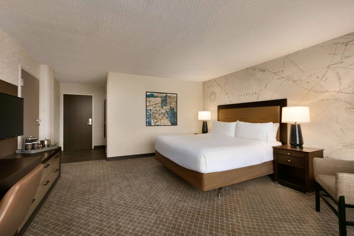 A hotel room with a large bed, two bedside tables with lamps, a flat-screen TV, a desk with a chair, and a map on the wall.