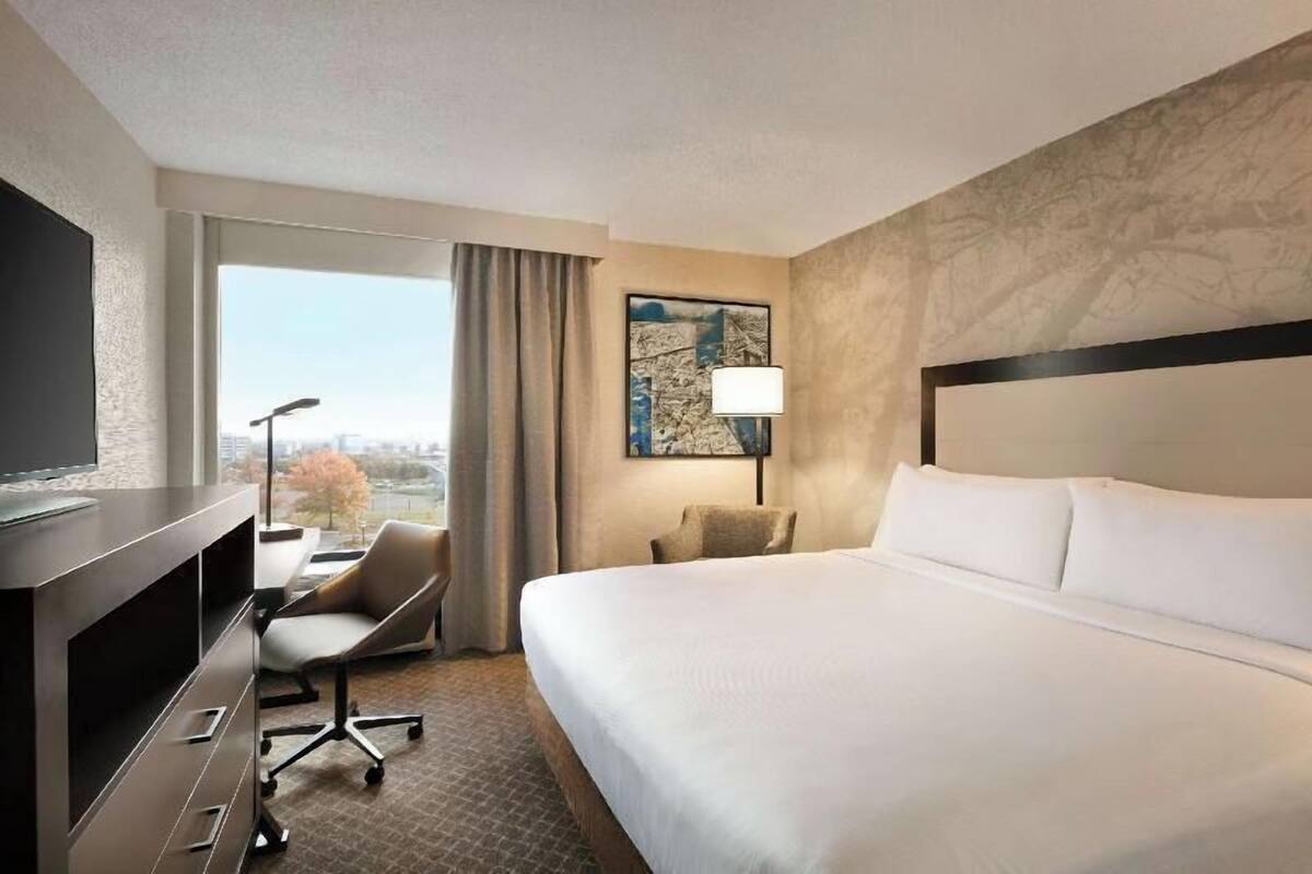A hotel room with a bed, desk, chair, and a city view.