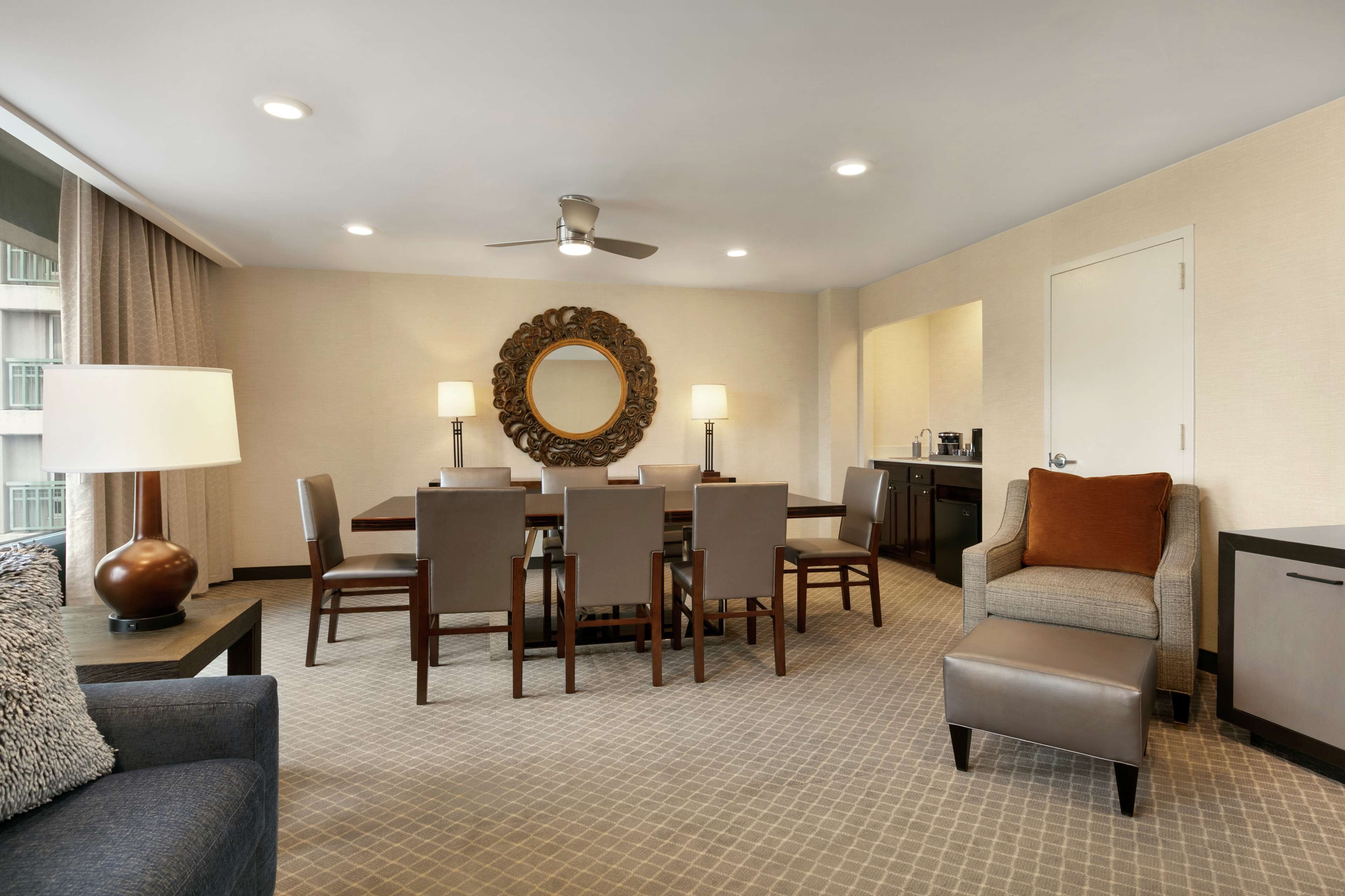 A hotel room with a dining area, a sofa, a coffee table, a TV, and a minibar.