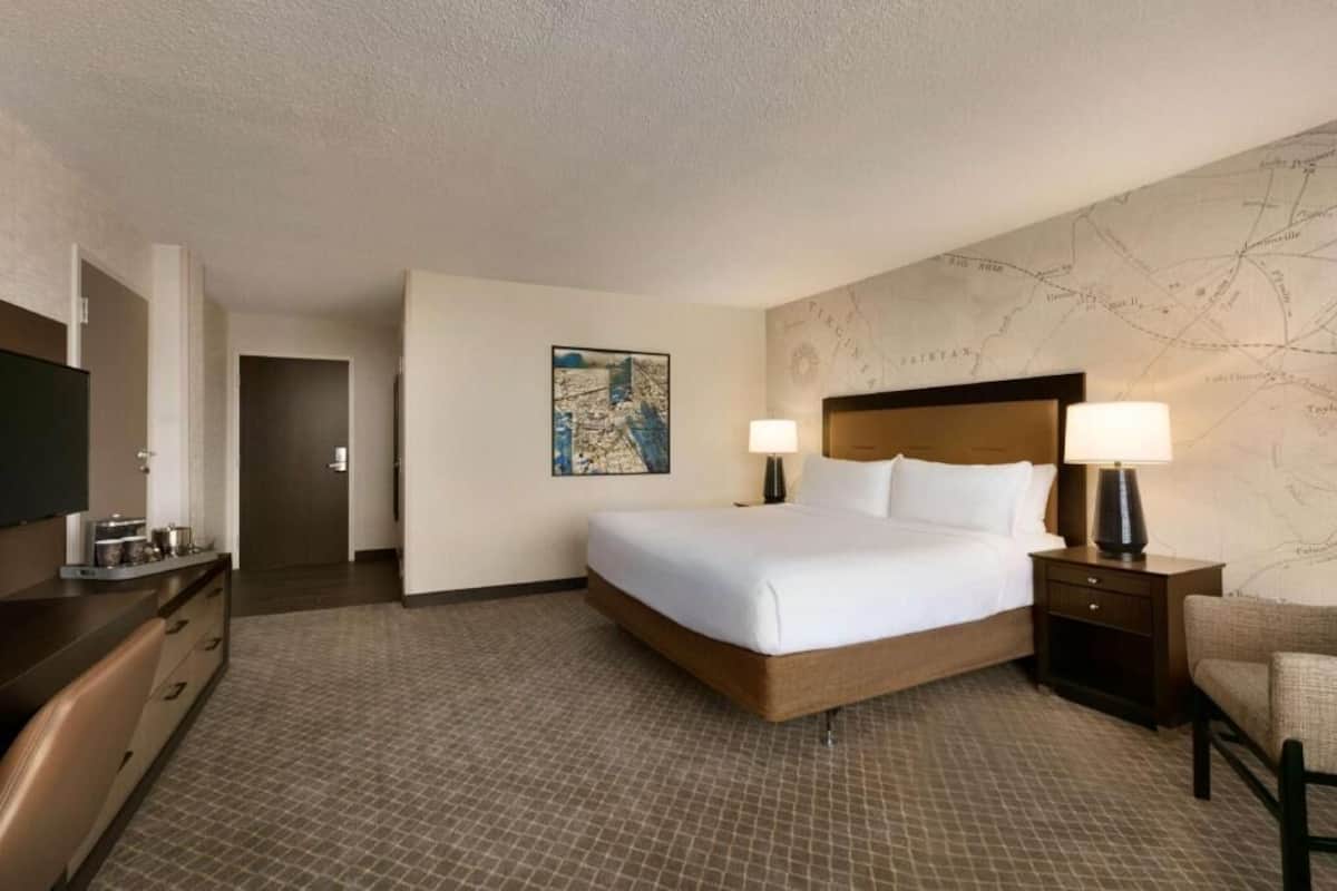 A hotel room with a bed, two bedside tables with lamps, a flat-screen TV, a dresser, and a map on the wall.