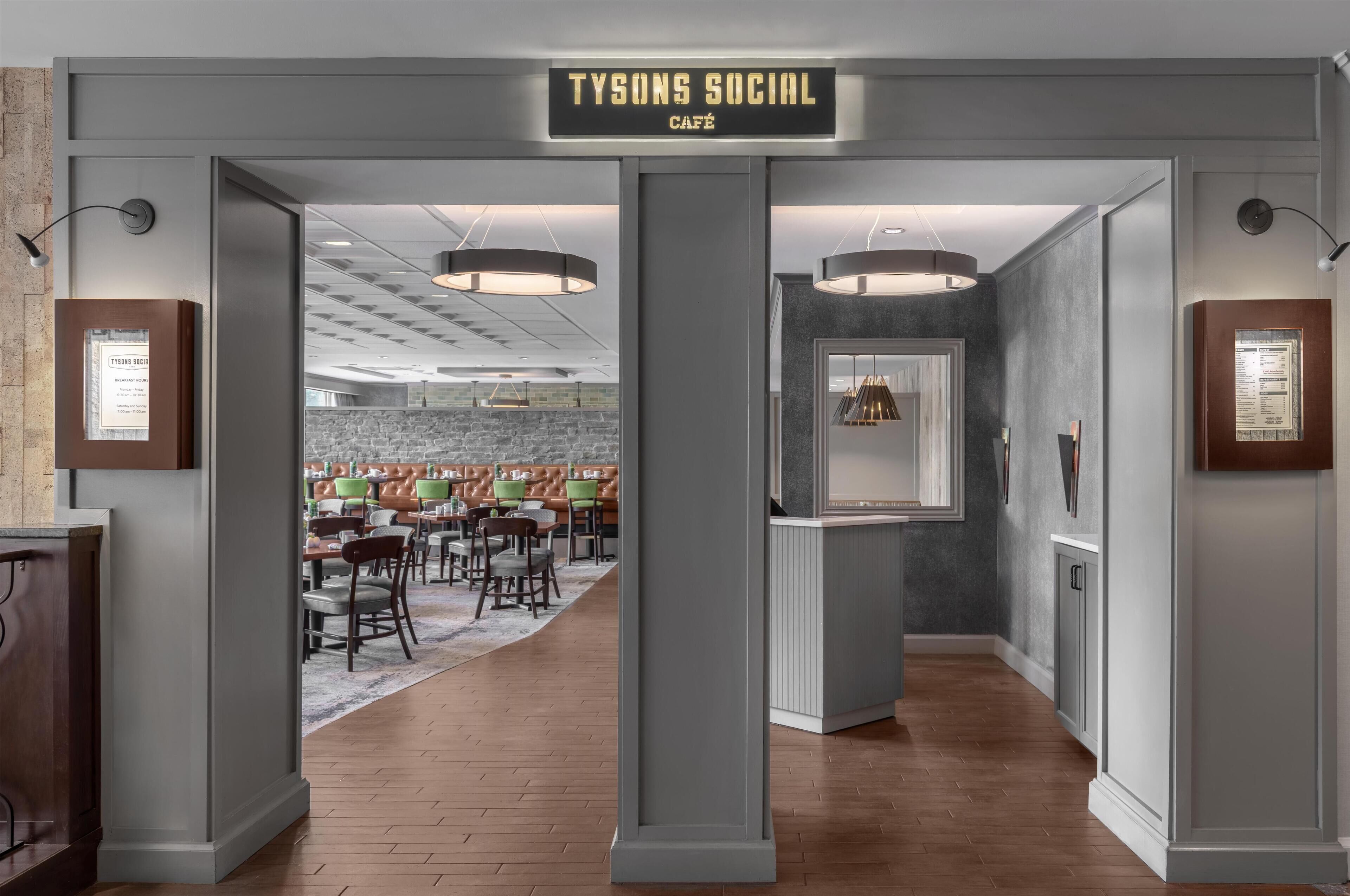 A modern interior with a sign reading "TYSONS SOCIAL CAFE" and a seating area with tables and chairs.
