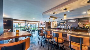 A modern bar area with wooden tables and orange chairs, a counter with a sign reading "TYSONS SOCIAL," and a view of the outdoors through large windows. - Doubletree by Hilton McLean Tysons (McLean)