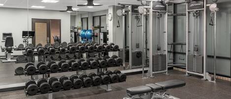 A gym with weightlifting equipment, a bench, and a mirrored wall.