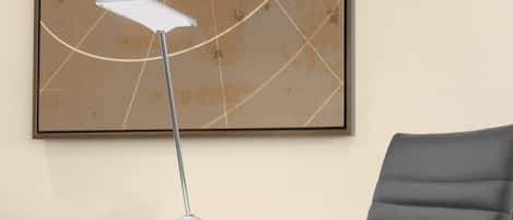 Una silla de oficina moderna con un respaldo alto y reposabrazos, un escritorio con una lámpara metálica y una obra de arte abstracta enmarcada en la pared.