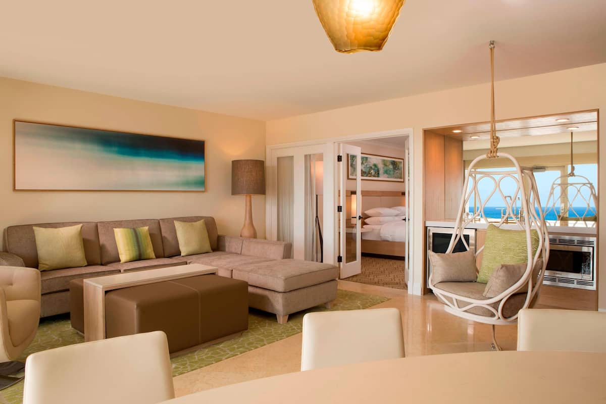 A modern hotel room with a sofa, ottoman, hanging chair, and a view of the sea.