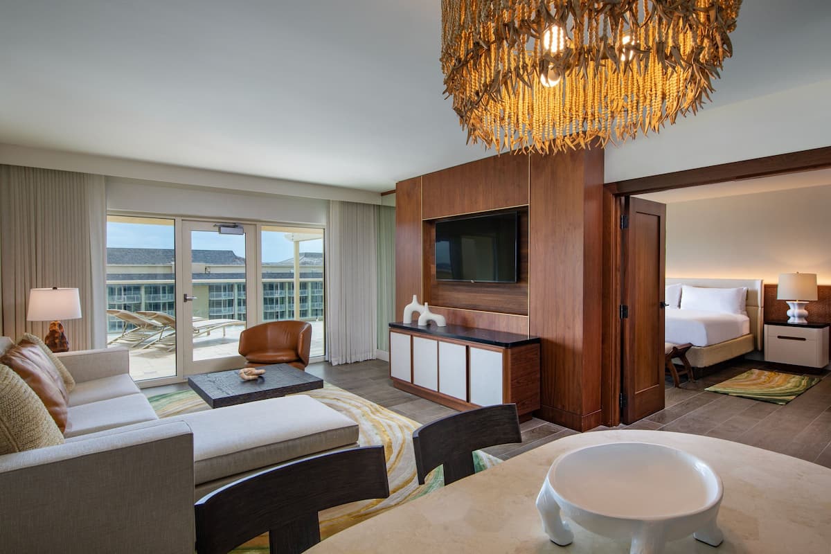 A hotel room with a sofa, dining table, TV, and a large window with a view.