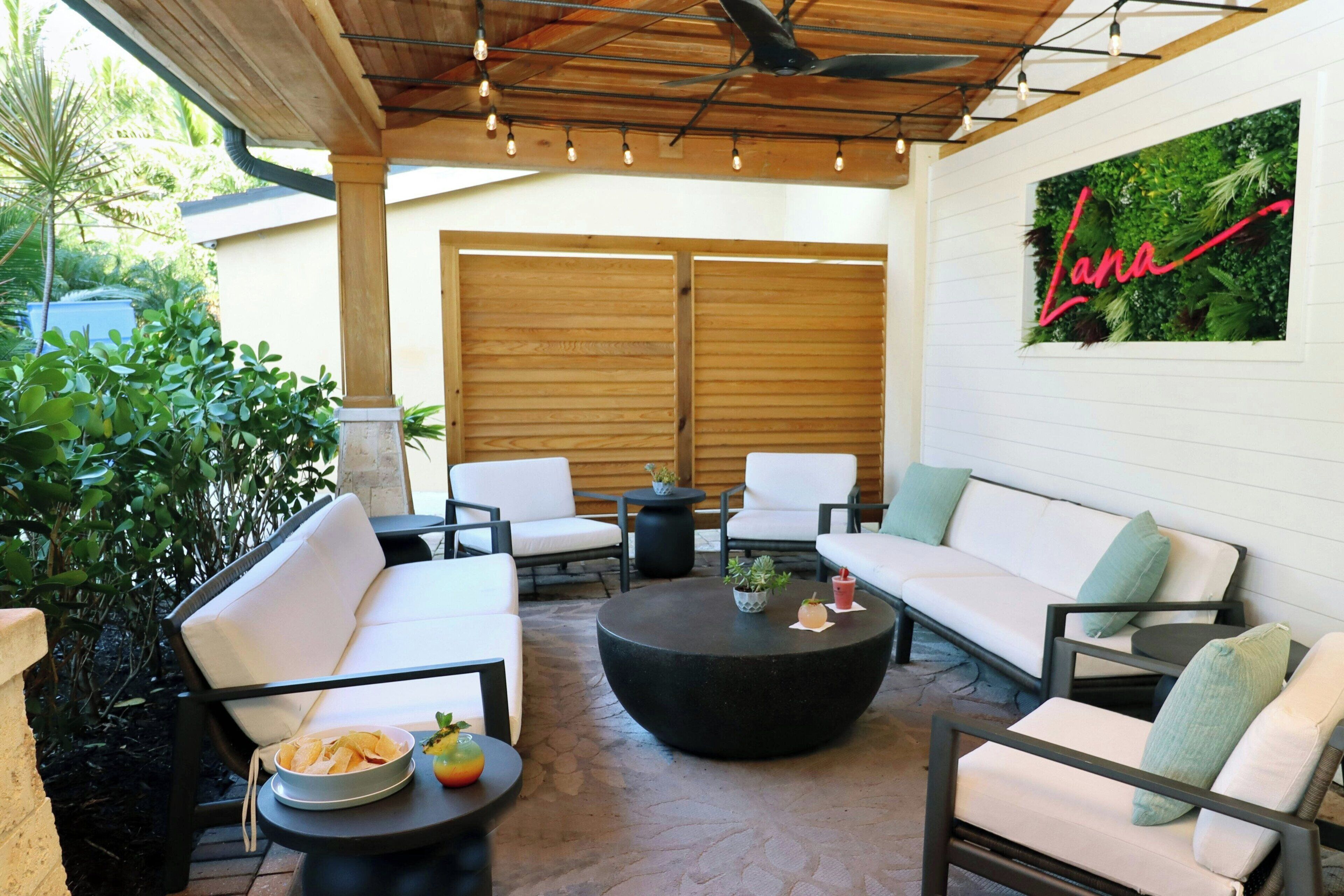 Un espace patio avec des canapés blancs, une table basse ronde noire et un plafond en bois avec des poutres apparentes et des luminaires suspendus.