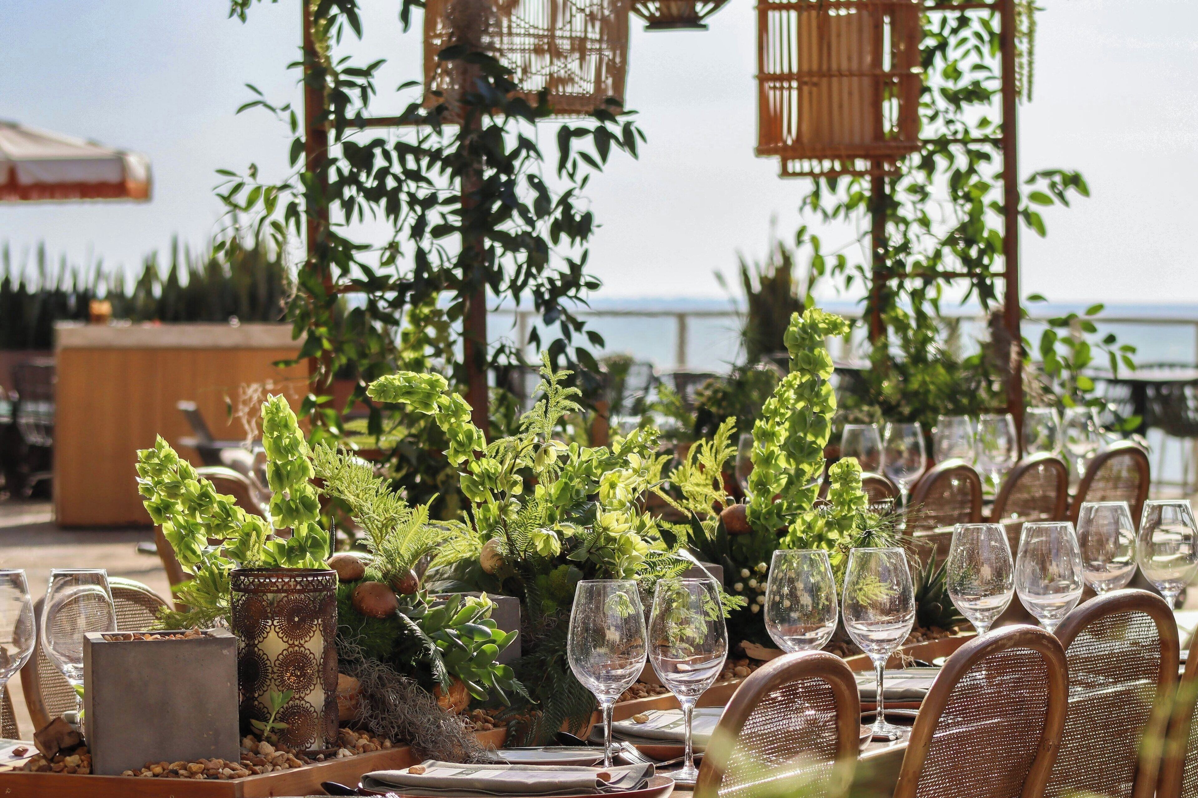 Un espace de restauration en plein air, avec des tables dressées pour le repas, entouré d’une végétation luxuriante et agrémenté de jardinières décoratives.