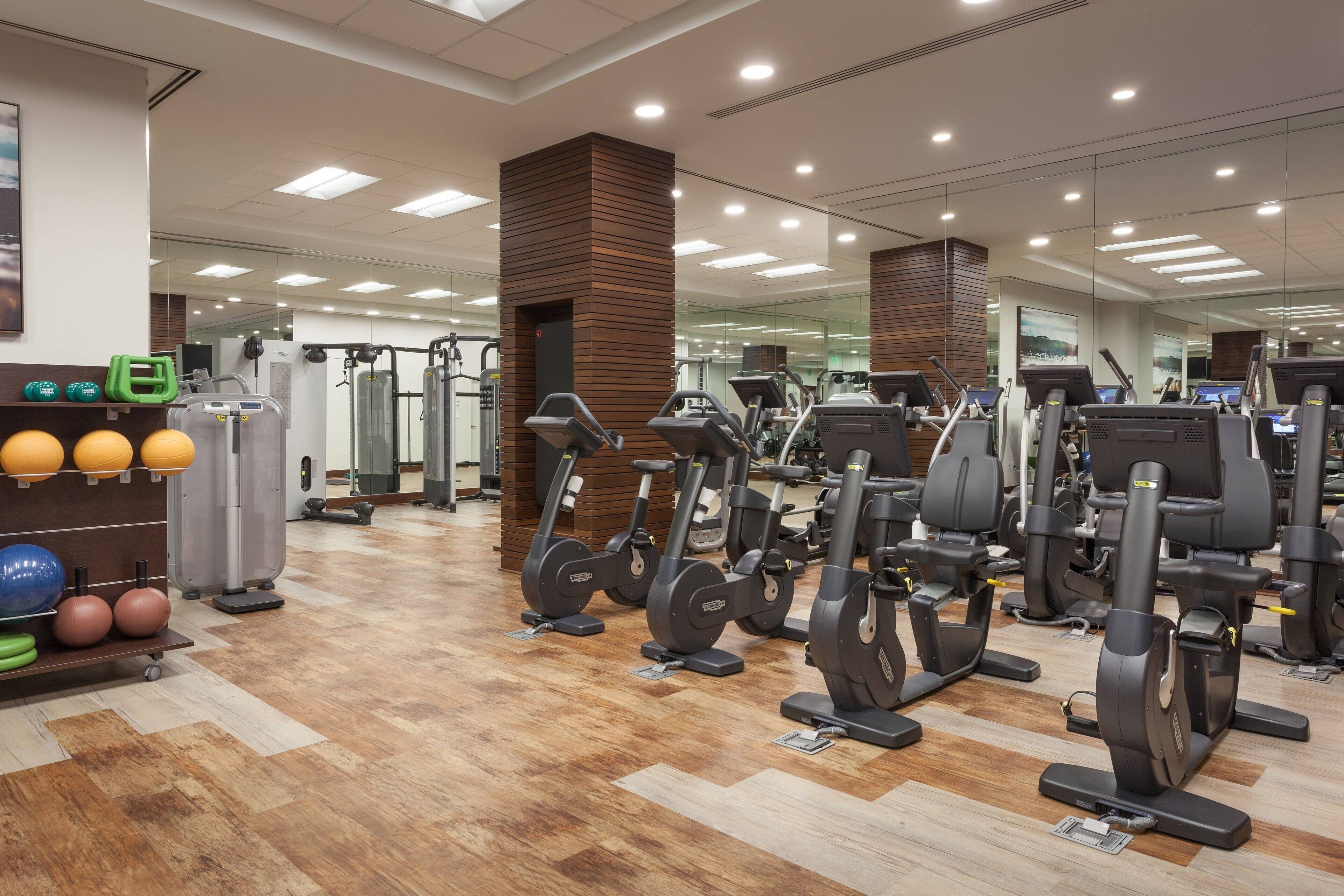 Een sportschool met trainingsapparatuur, een houten vloer en een spiegelwand.