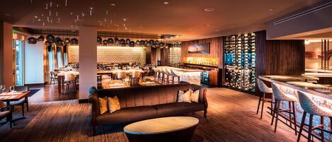 Un espace bar moderne avec un comptoir en bois, des sièges et un grand écran.