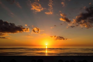 Pôr do sol sobre uma praia com céu limpo e mar calmo.
