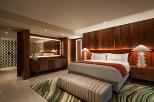 Quarto de hotel moderno com uma cama grande, uma mesinha de arrumar com espelho e uma parede de destaque em madeira.