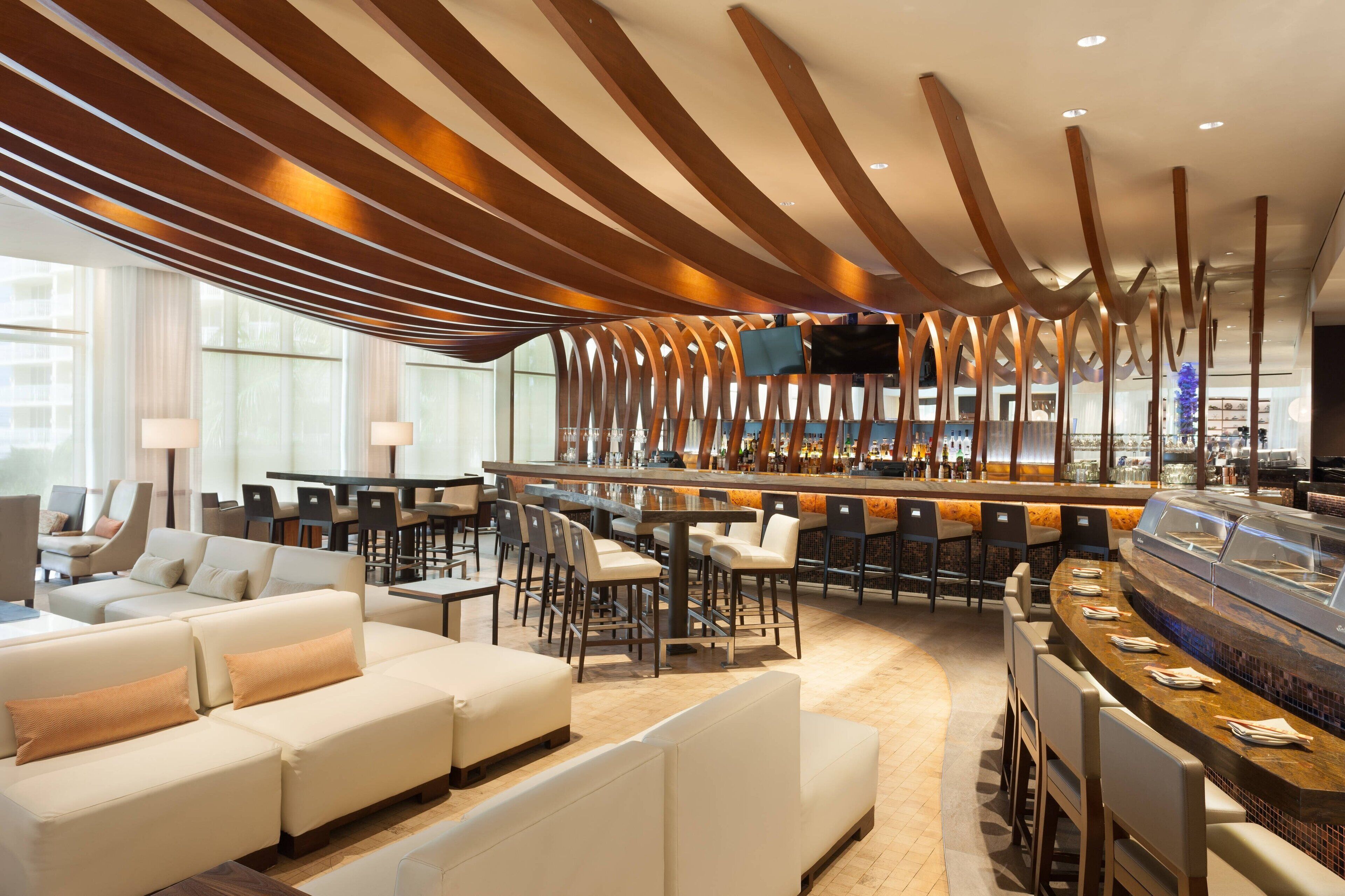 Un moderno vestíbulo de hotel con una zona de bar, espacios para sentarse y un amplio ventanal que proporciona luz natural.