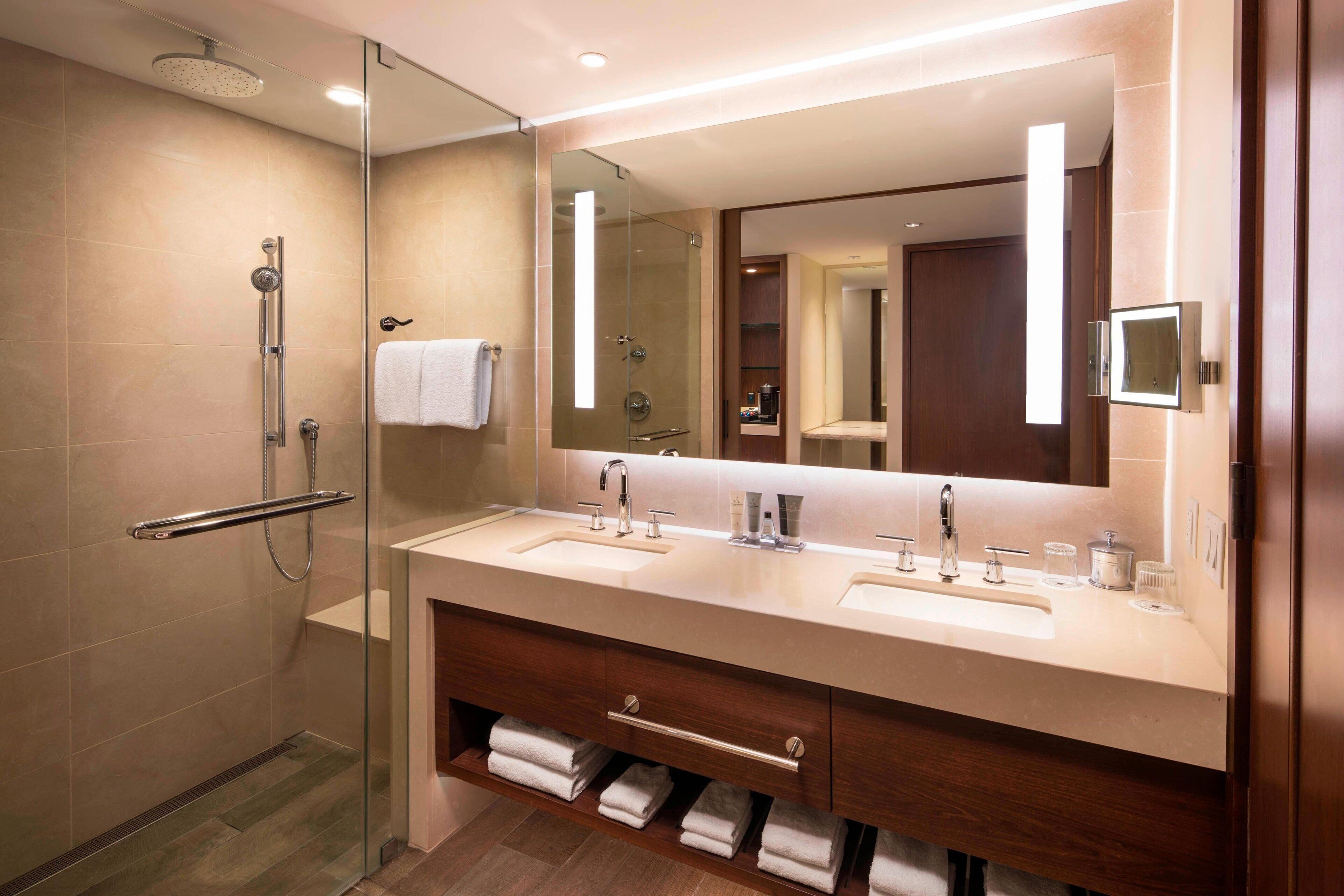 Un bagno moderno con cabina doccia in vetro, doppio lavabo e un grande specchio.