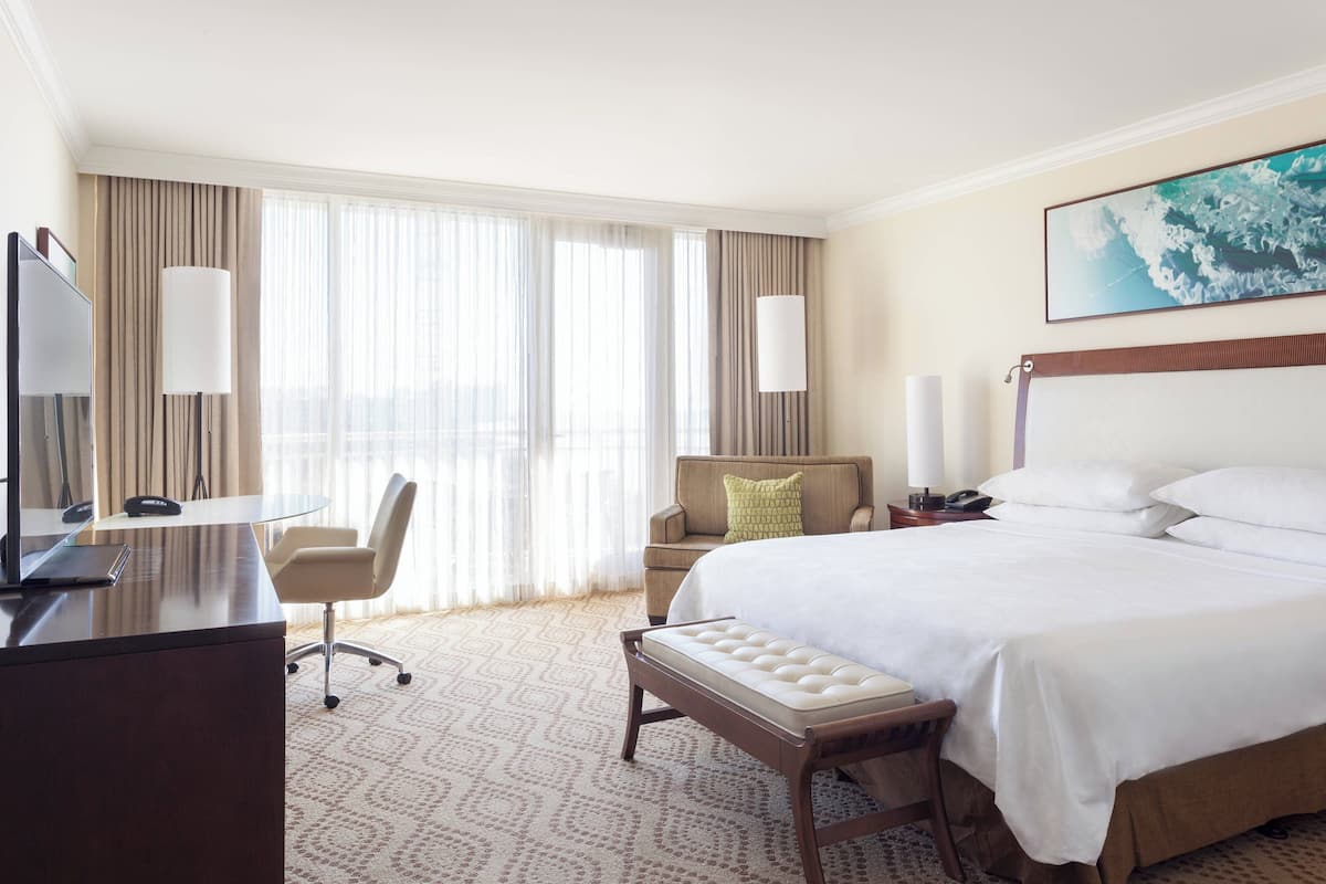 A hotel room with a bed, a desk, a chair, and a large window with curtains.