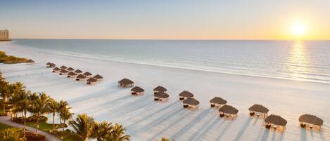 A beach resort with rows of thatched umbrellas and palm trees.