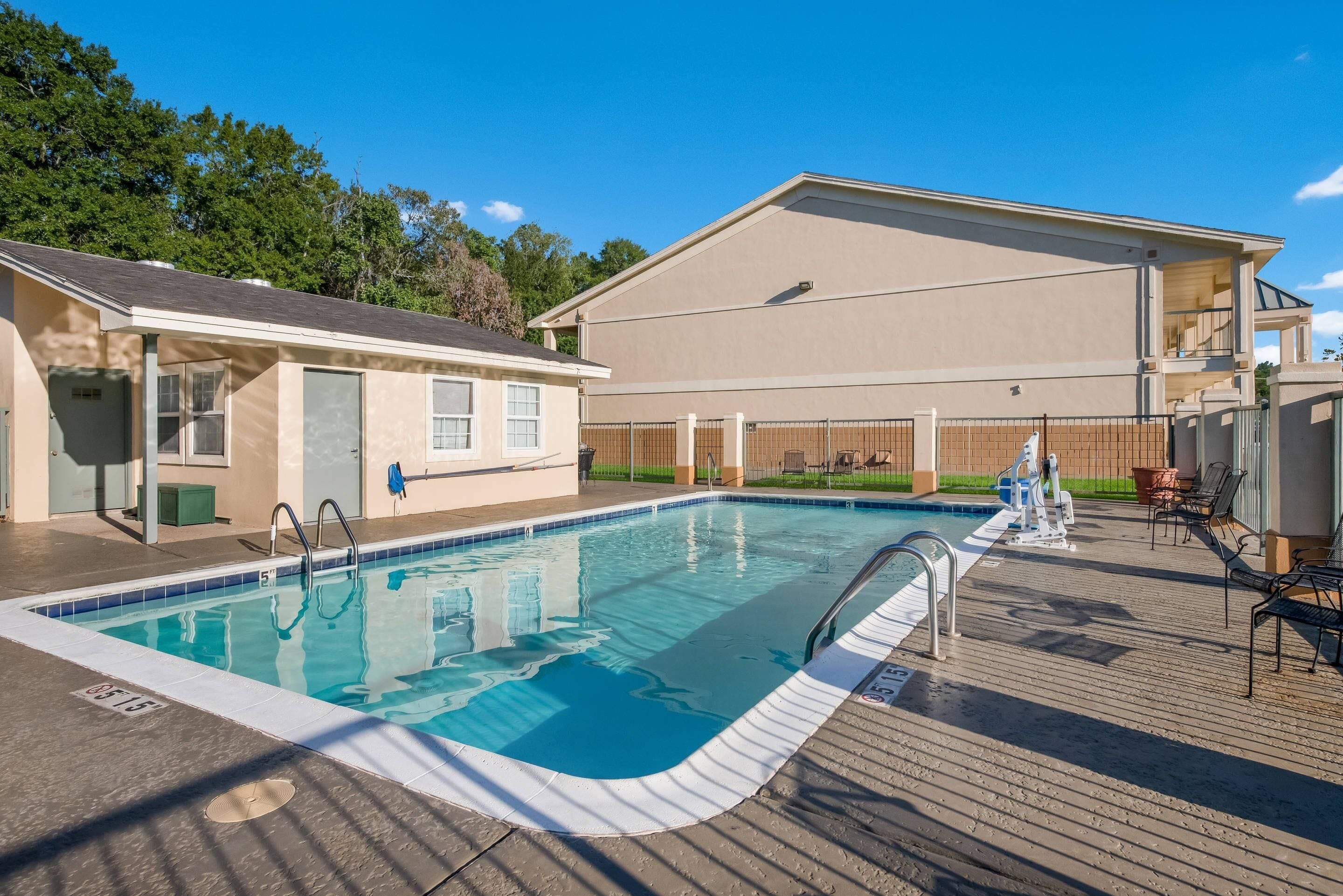 A swimming pool with a deck, a covered area, and a building in the background.