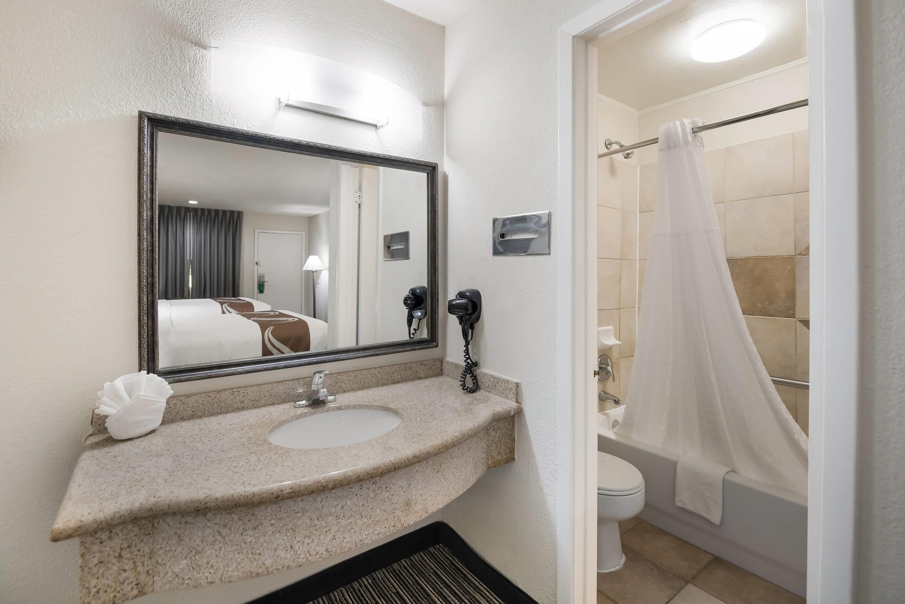 Un baño con lavamanos, espejo, inodoro y cortina de ducha.