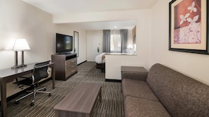 Una habitación de hotel con escritorio, silla, televisor, sofá y cama con cortinas.