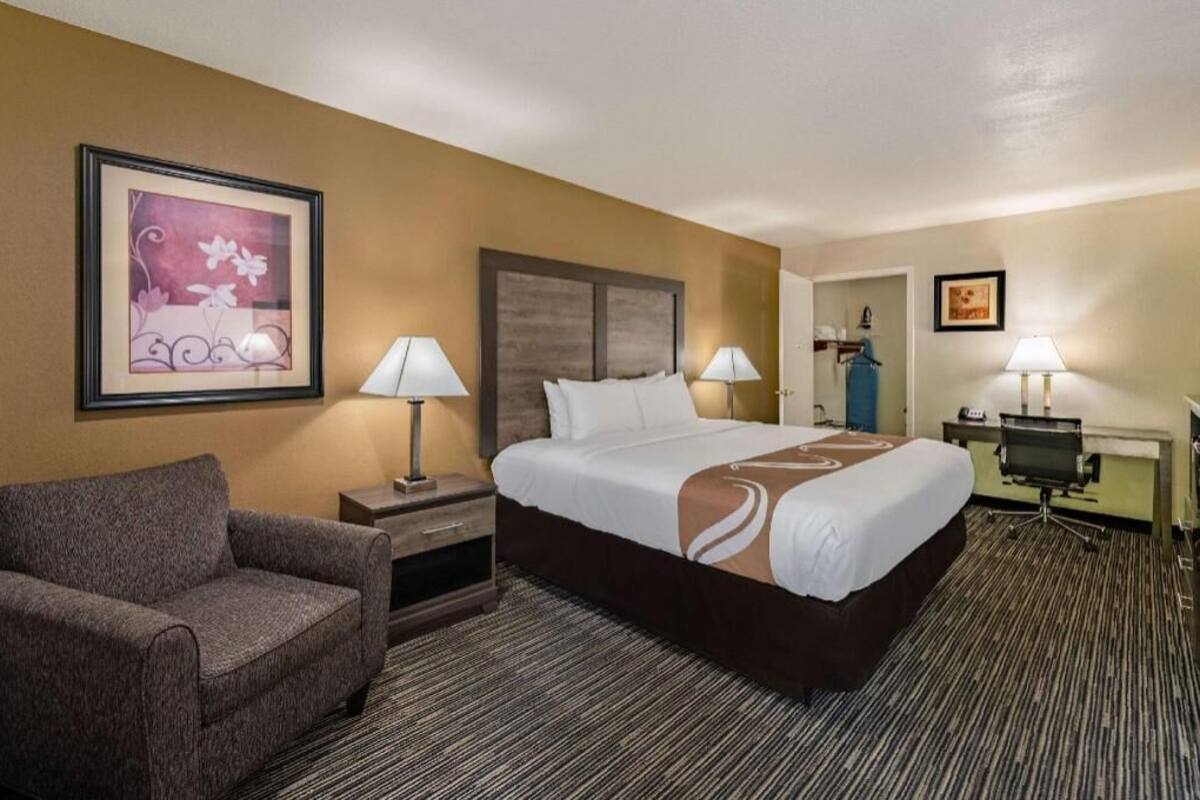A hotel room with a large bed, two bedside lamps, a chair, a desk, and a framed picture on the wall.